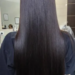 Długie, ciemne, idealnie proste włosy po zabiegu wygładzania keratynowego, widok z tyłu na tle salonu. Połyskujące, zdrowo wyglądające pasma.