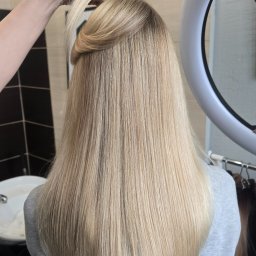 Alena Semiantsova - Salon fryzjerski, Fryzjer Warszawa - Blond włosy po koloryzacji AirTouch. Subtelne przejścia kolorów, naturalny efekt. W tle ring doświetlający i wieszak z doczepianymi pasmami włosów. Fryzjer.
