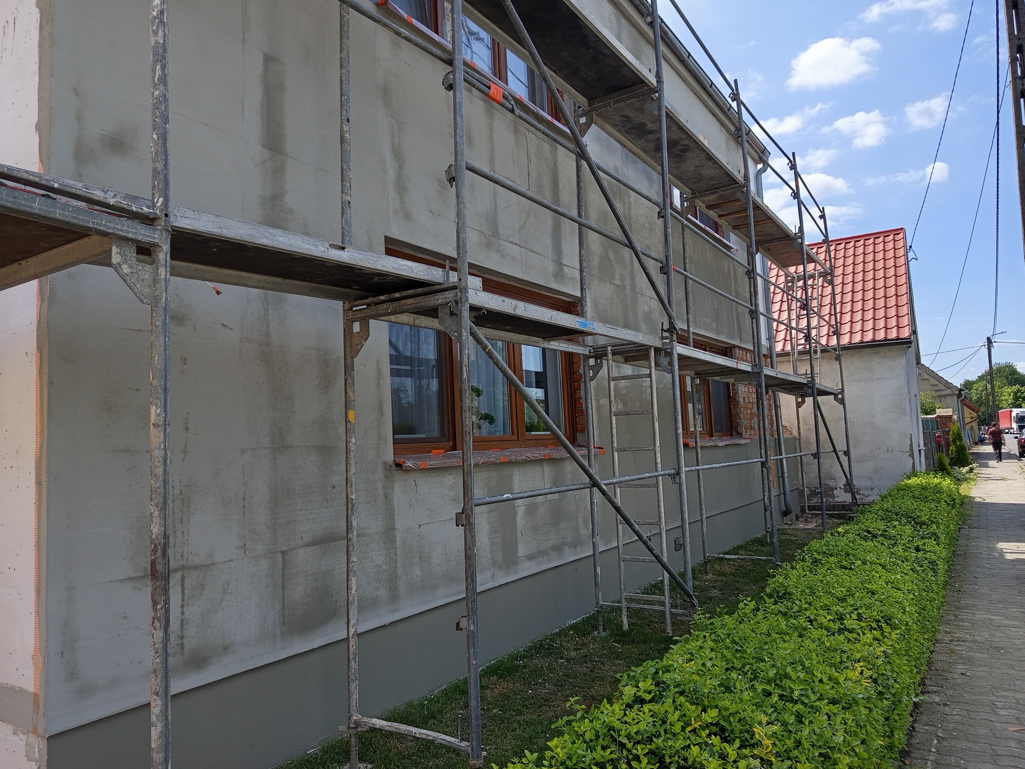 Elewacja domu w trakcie szpachlowania, widoczne rusztowania i fragment ściany z nałożoną warstwą szpachli, tło stanowi niebieskie niebo.