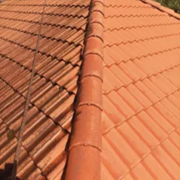 Częściowo umyty dach z czerwonej dachówki ceramicznej, widoczne zabrudzenia po lewej stronie i czysta powierzchnia po prawej. Perspektywa z góry, widoczny fragment liny.