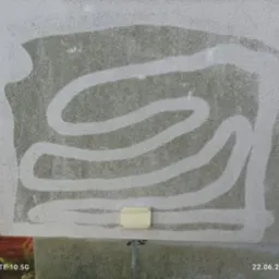 Fragment elewacji z widocznym efektem czyszczenia, ukazującym kontrast między umytą a zabrudzoną powierzchnią. Widoczny wzór czyszczenia i niewielki element instalacji.