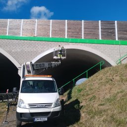 Drew-Wart - Pracownik w koszu podnośnika czyści tunel drogowy. Biały samochód Iveco z podnośnikiem koszowym na tle tunelu i niebieskiego nieba.
