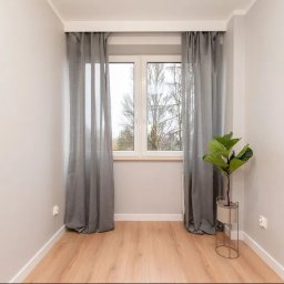 KLIMAR MICHAŁ CHMIEL - Jasne wnętrze po remoncie: świeżo pomalowane ściany, drewniana podłoga, okno z szarymi zasłonami i roślina w minimalistycznej donicy.