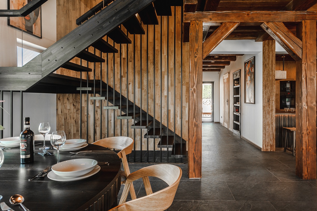 Nowoczesne schody z drewnianymi elementami w przestronnym wnętrzu domu w Lesku. Widoczny stół z zastawą i dekoracyjne oświetlenie, tworzące przytulny klimat.