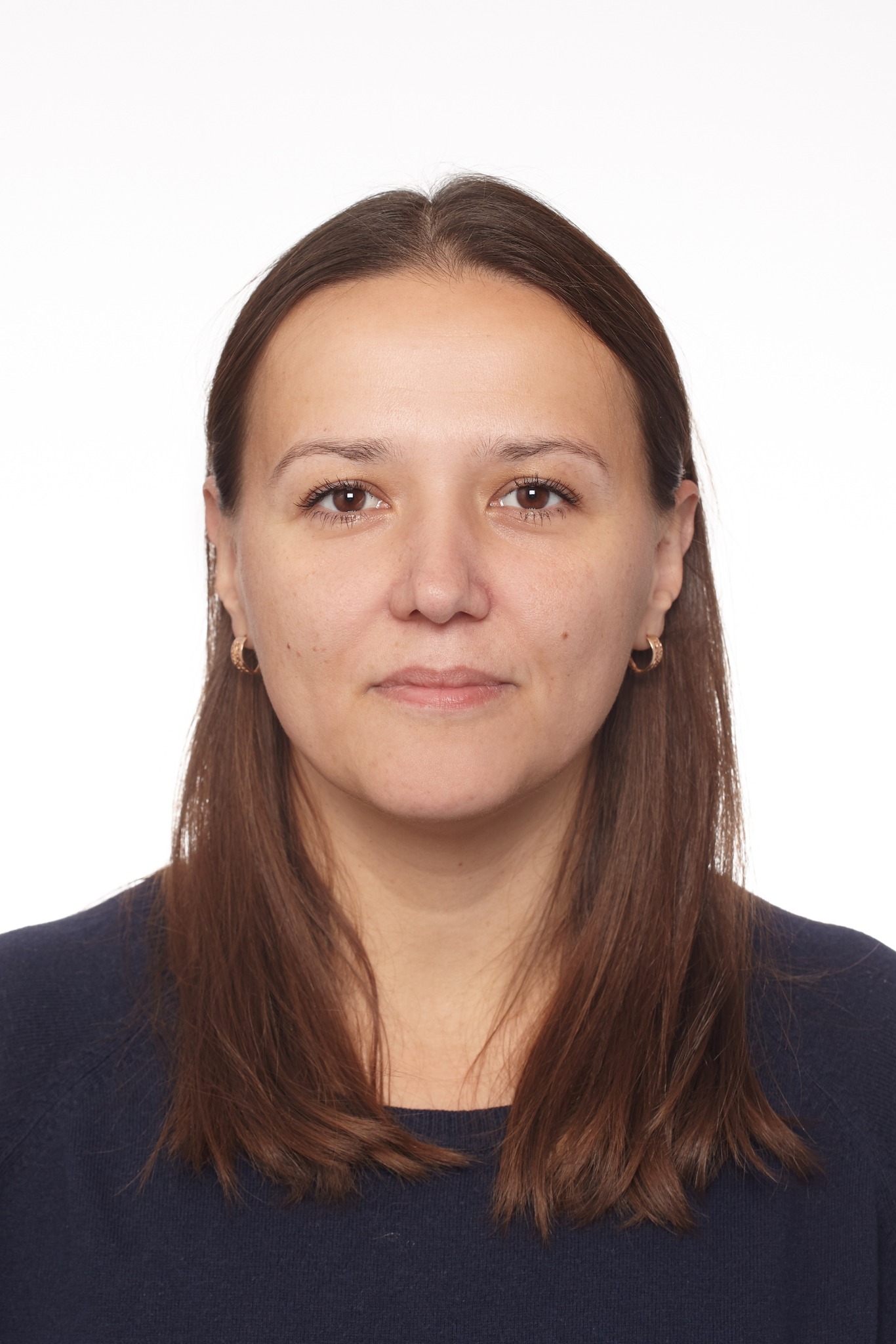 Portret kobiety z brązowymi włosami, ubranej w granatową bluzkę, na białym tle. Widoczne złote kolczyki. Neutralny wyraz twarzy, bezpośrednie spojrzenie.