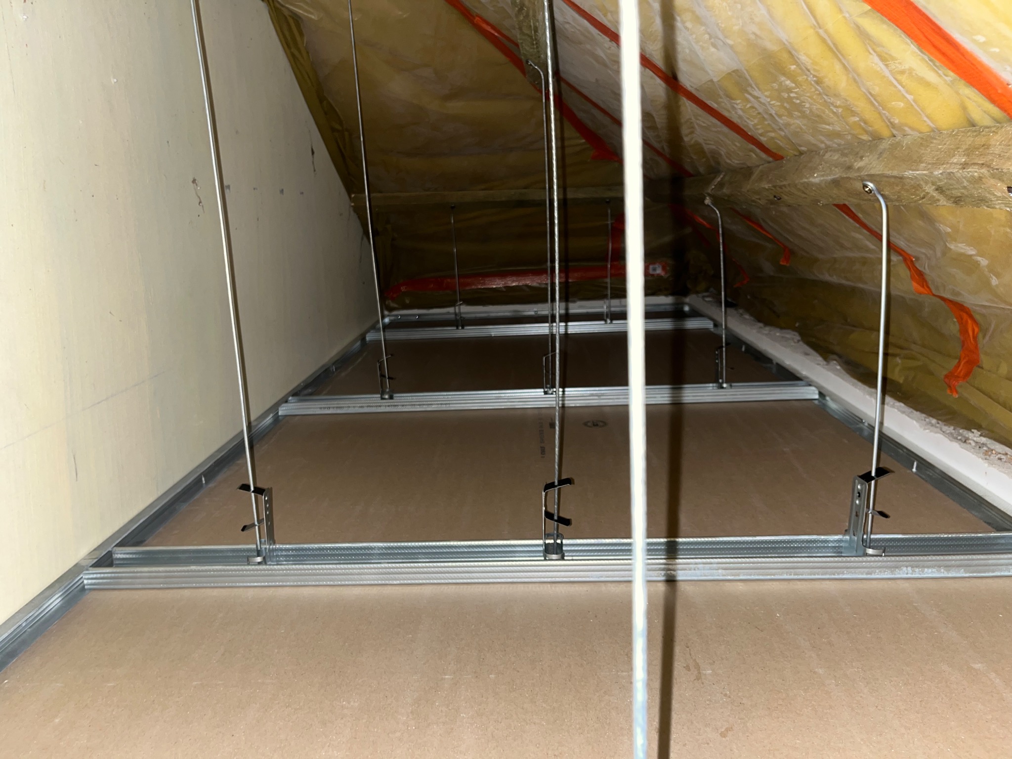 Montaż sufitu podwieszanego z płyt karton-gips na poddaszu. Widoczne profile, zawiesia i izolacja termiczna. Ujęcie z dołu, perspektywa wnętrza poddasza.