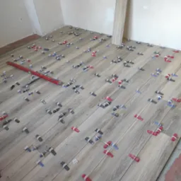 Układanie podłogi z płytek imitujących drewno, z użyciem poziomicy i klipsów poziomujących. Widoczne surowe ściany i fragment ułożonej płytki przy ścianie.