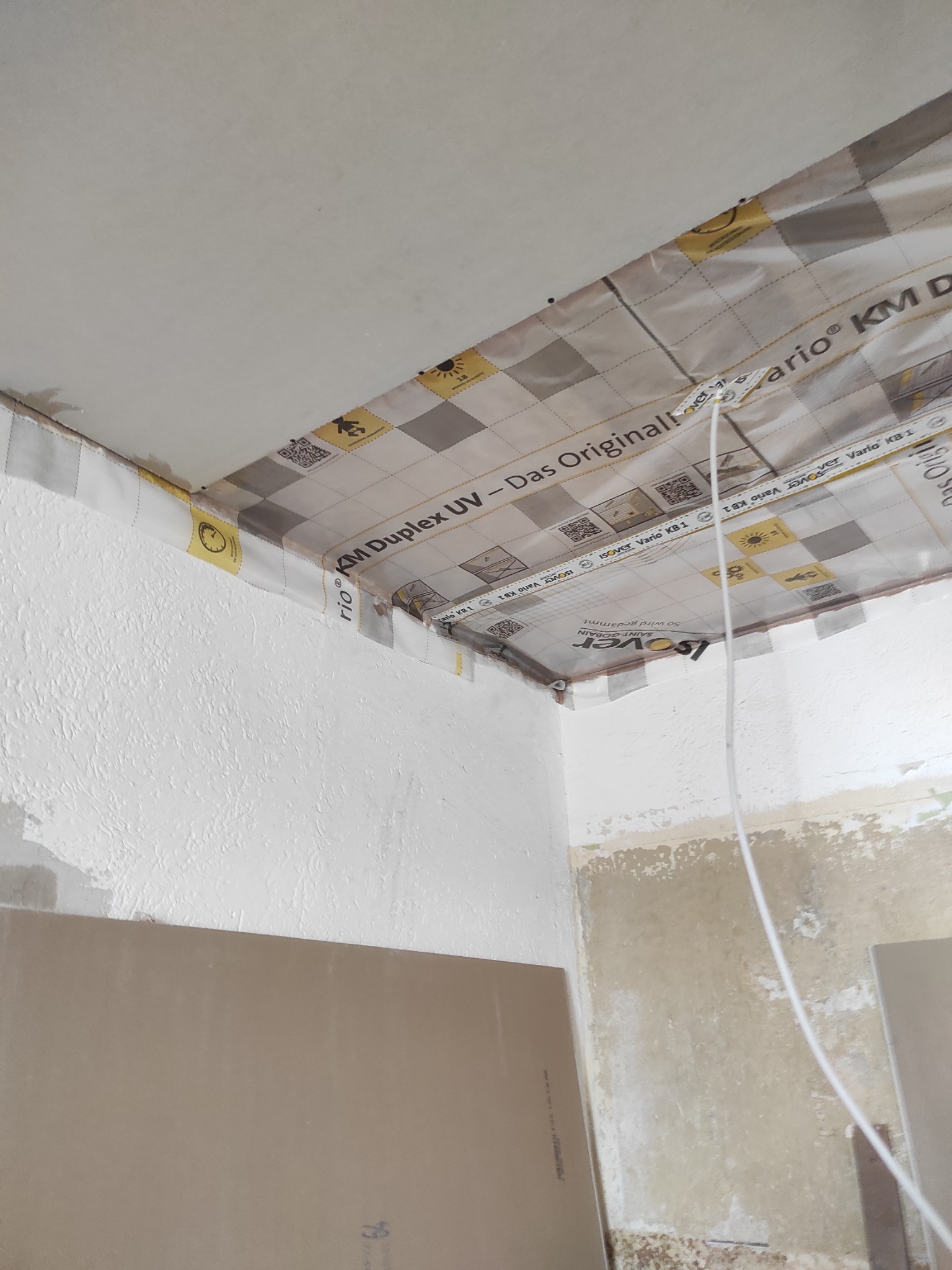 Montaż folii paroizolacyjnej Isover Vario KB1 na suficie podwieszanym, widoczne elementy konstrukcji i surowa ściana. Etap prac wykończeniowych w pomieszczeniu.