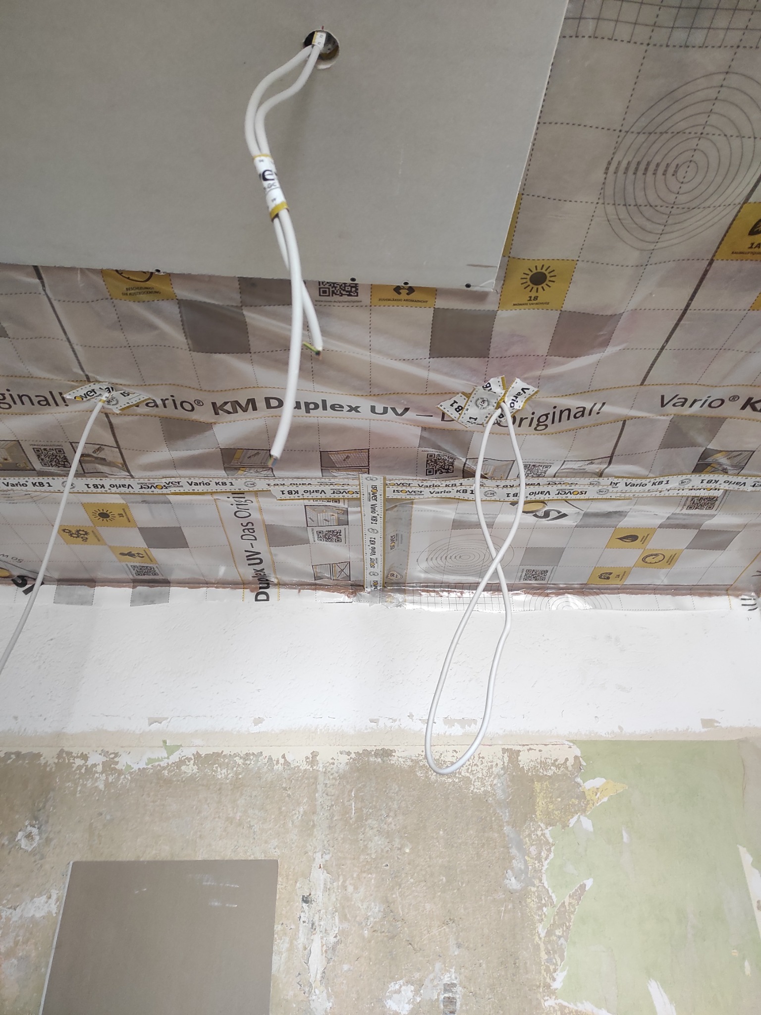 Montaż sufitu podwieszanego z widocznymi kablami i folią paroizolacyjną Vario KM Duplex UV, ukazujący etap prac wykończeniowych wnętrza.