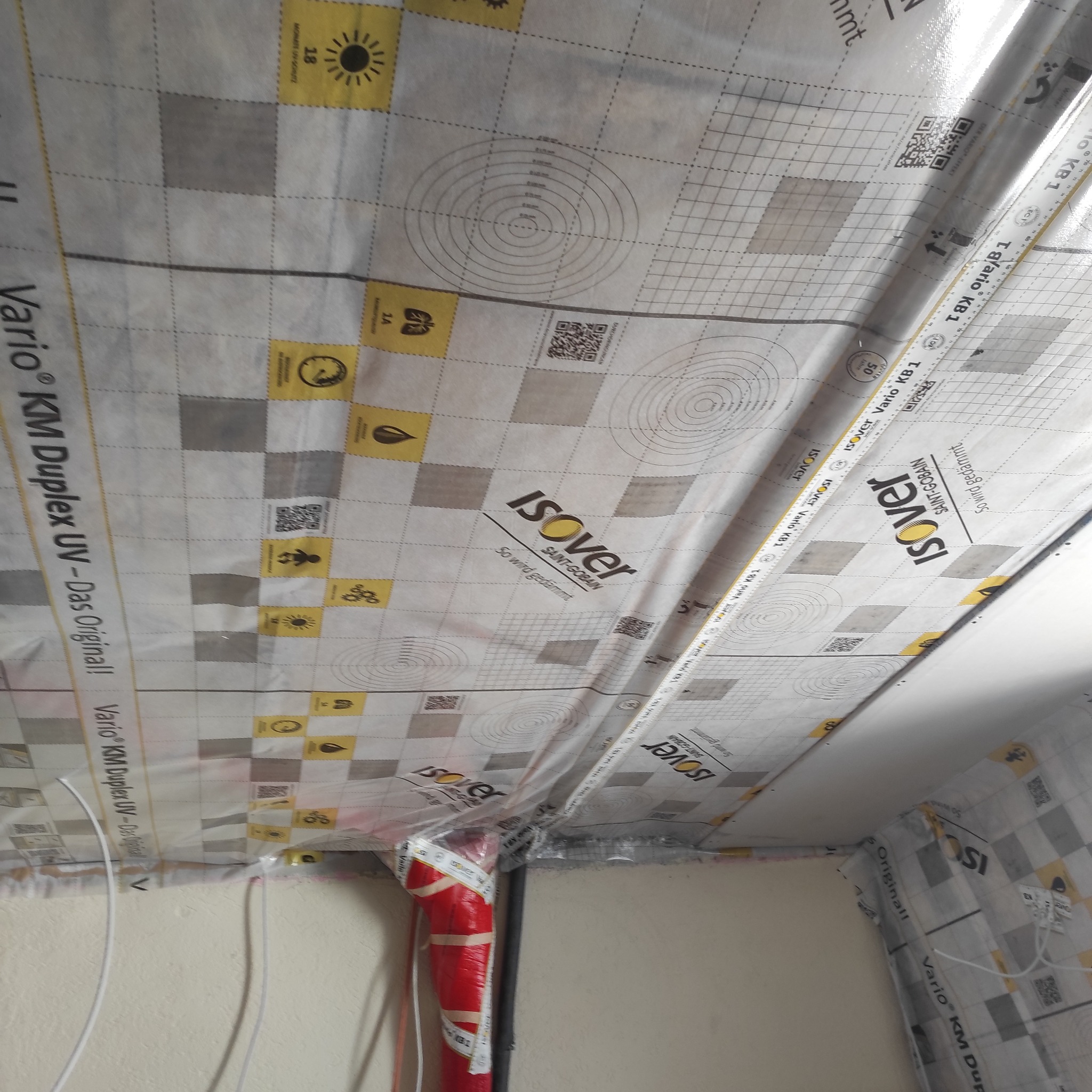 Folia paroizolacyjna Isover Vario KM Duplex UV na suficie, z widocznymi oznaczeniami i liniami pomocniczymi, zamontowana na styku ściany i sufitu.