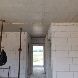 Ivan Harmash - Wnętrze w trakcie budowy: ściany z betonu komórkowego, stalowe podpory, widok na zewnątrz przez otwory drzwiowe. Surowy stan, w tle zieleń.