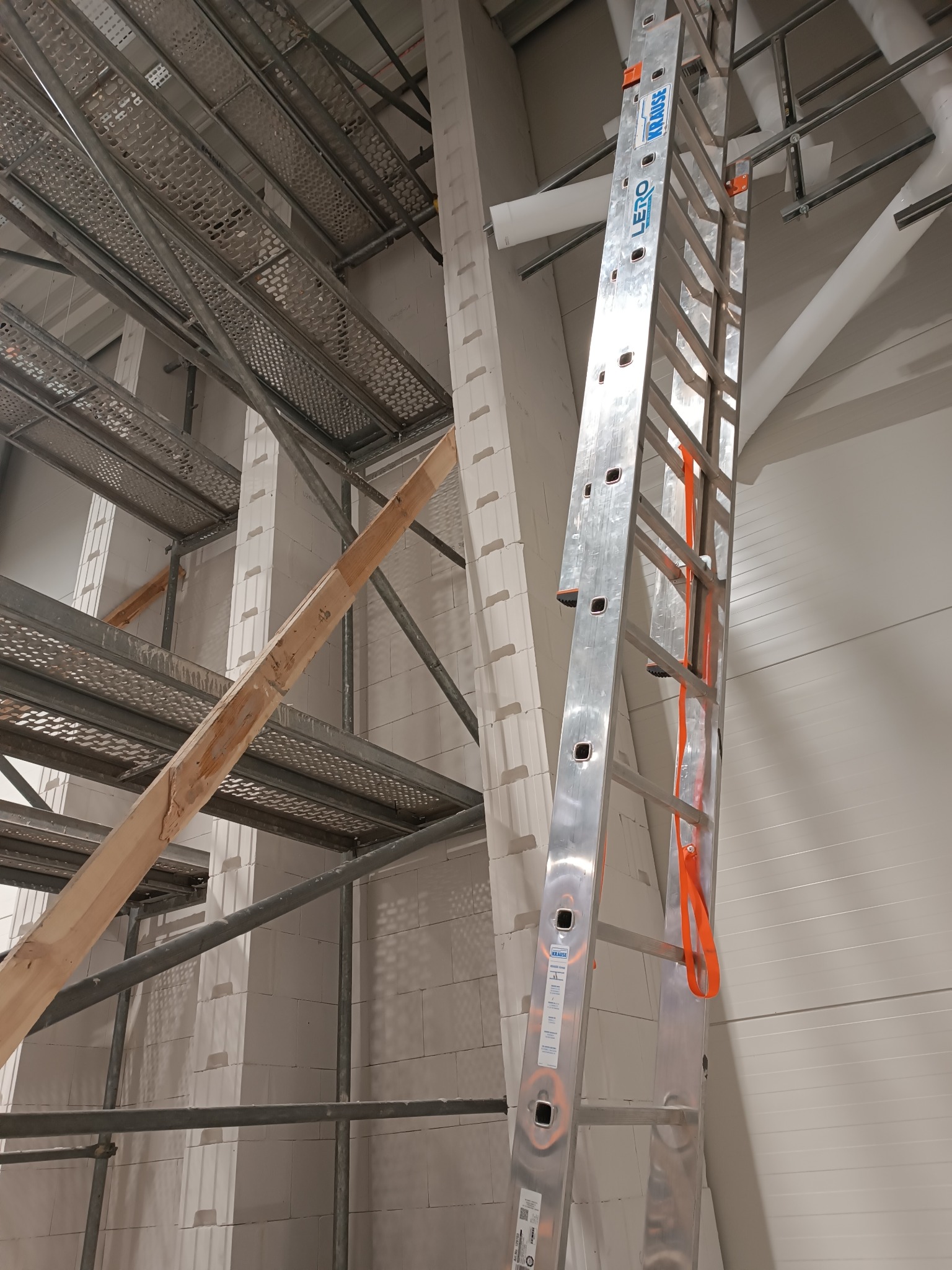 Wnętrze w trakcie murowania ścian z białych bloczków. Widoczne rusztowania, drabina Krause i drewniana belka. Ściany z betonu komórkowego.