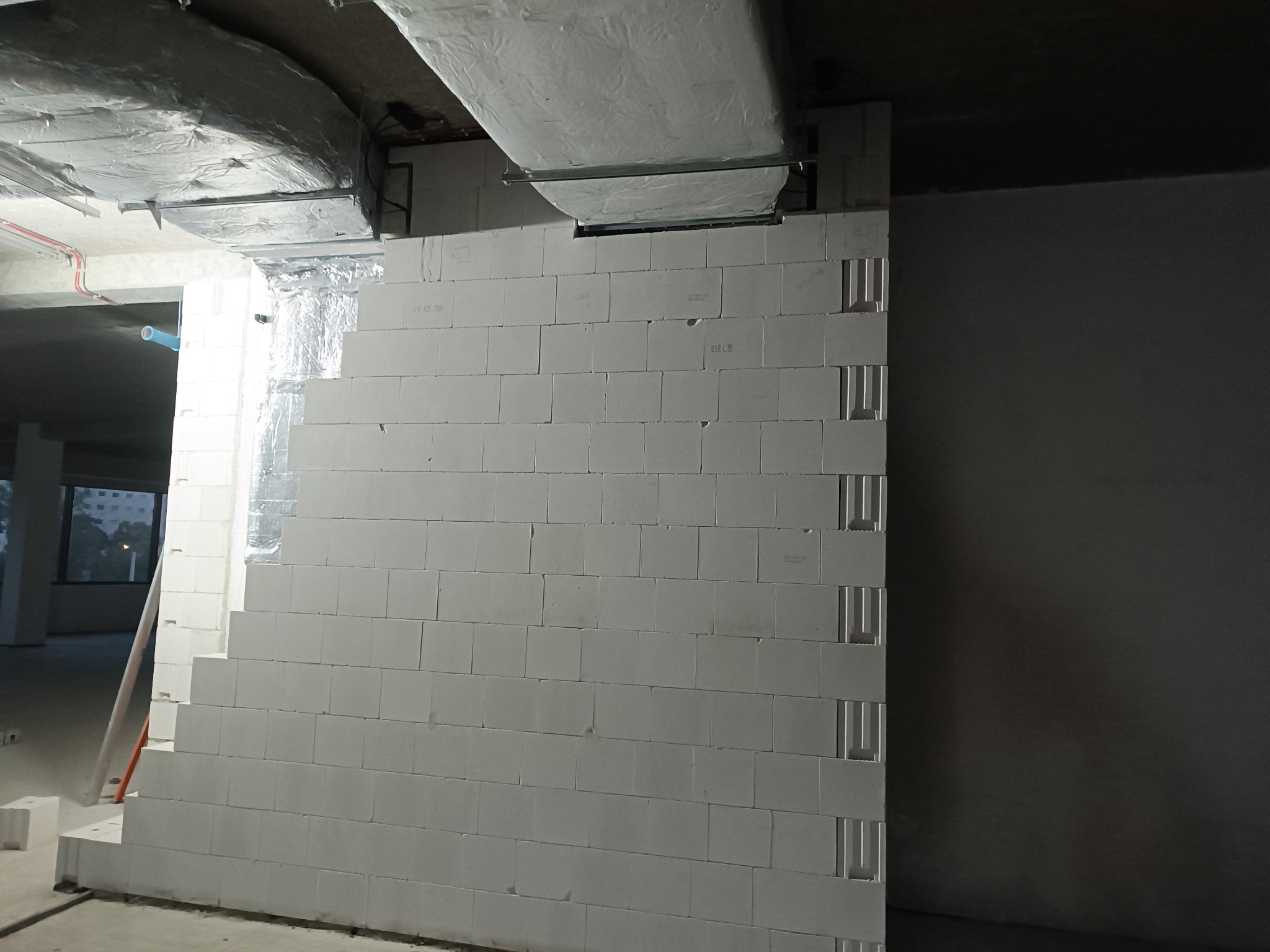 Wznoszenie ściany z bloczków betonu komórkowego Ytong w Bielawie. Widoczne elementy wentylacji pod sufitem i fragment okna w tle. Etap budowy.