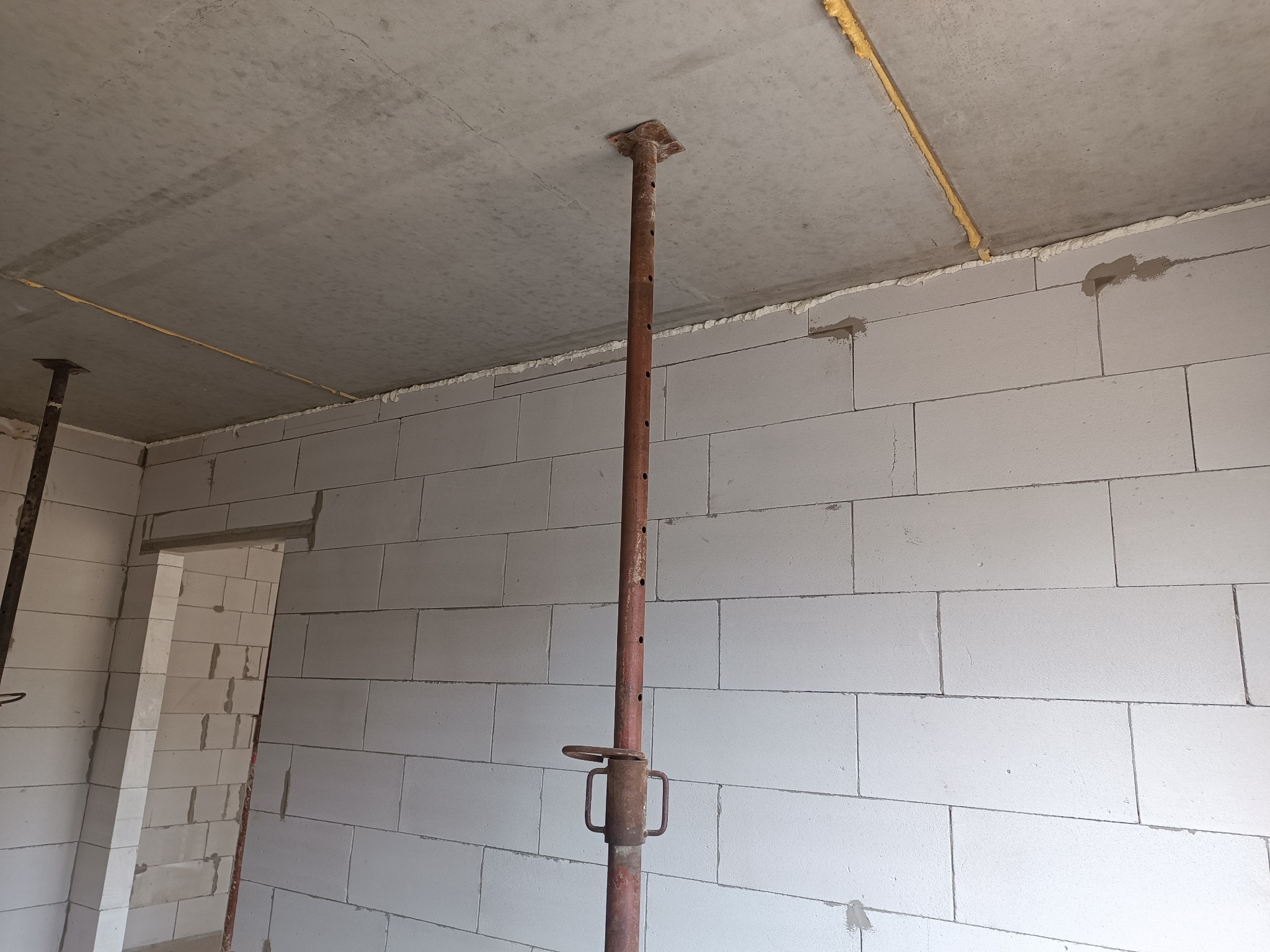 Wnętrze w trakcie budowy z białych bloczków, z widocznym stemplem budowlanym podtrzymującym strop i pianką montażową w szczelinach.