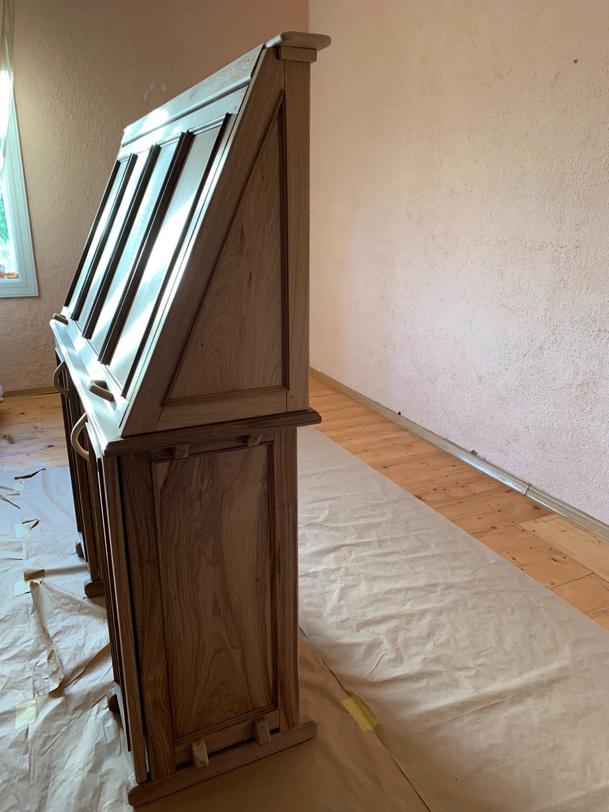 Antyczny sekretarzyk z drewna orzechowego, po renowacji, zabezpieczony papierem malarskim. Widok z boku, ukazujący detale rzemiosła i odnowioną powierzchnię.