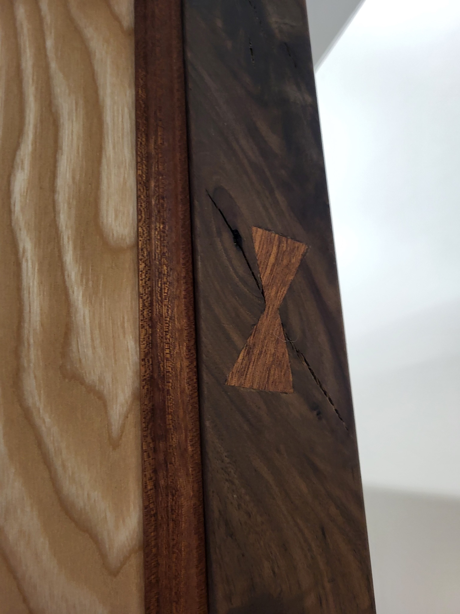 Detale łączenia drewna z motywem motyla na ciemnym drewnie, jasne drewno w tle. Widoczne słoje drewna i naturalne pęknięcia. Precyzyjna praca.