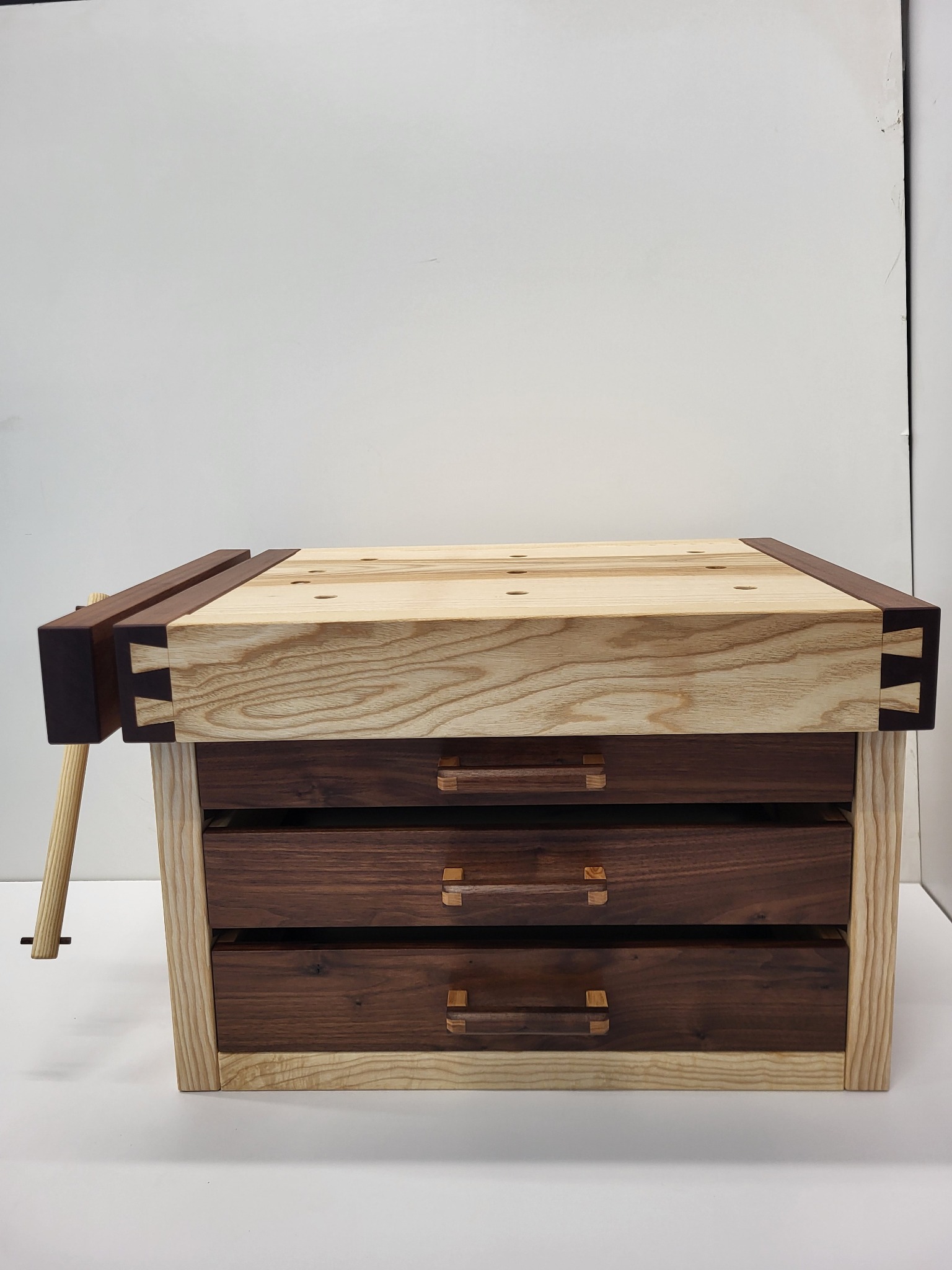 Drewniany stół warsztatowy z trzema szufladami, widoczne połączenia na czopy, jasne i ciemne drewno, na białym tle.