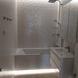 Glazrem - Nowoczesna łazienka w bieli: geometryczne płytki 3D, podświetlana wanna i szafka umywalkowa. Minimalistyczny design z chromowaną armaturą i akcesoriami.