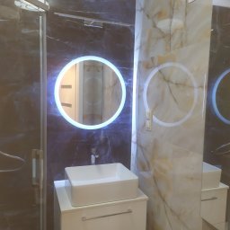 Glazrem - Nowoczesna łazienka z umywalką nablatową, podświetlanym lustrem i marmurowymi płytkami. Kabina prysznicowa ze szklanymi drzwiami po lewej stronie.