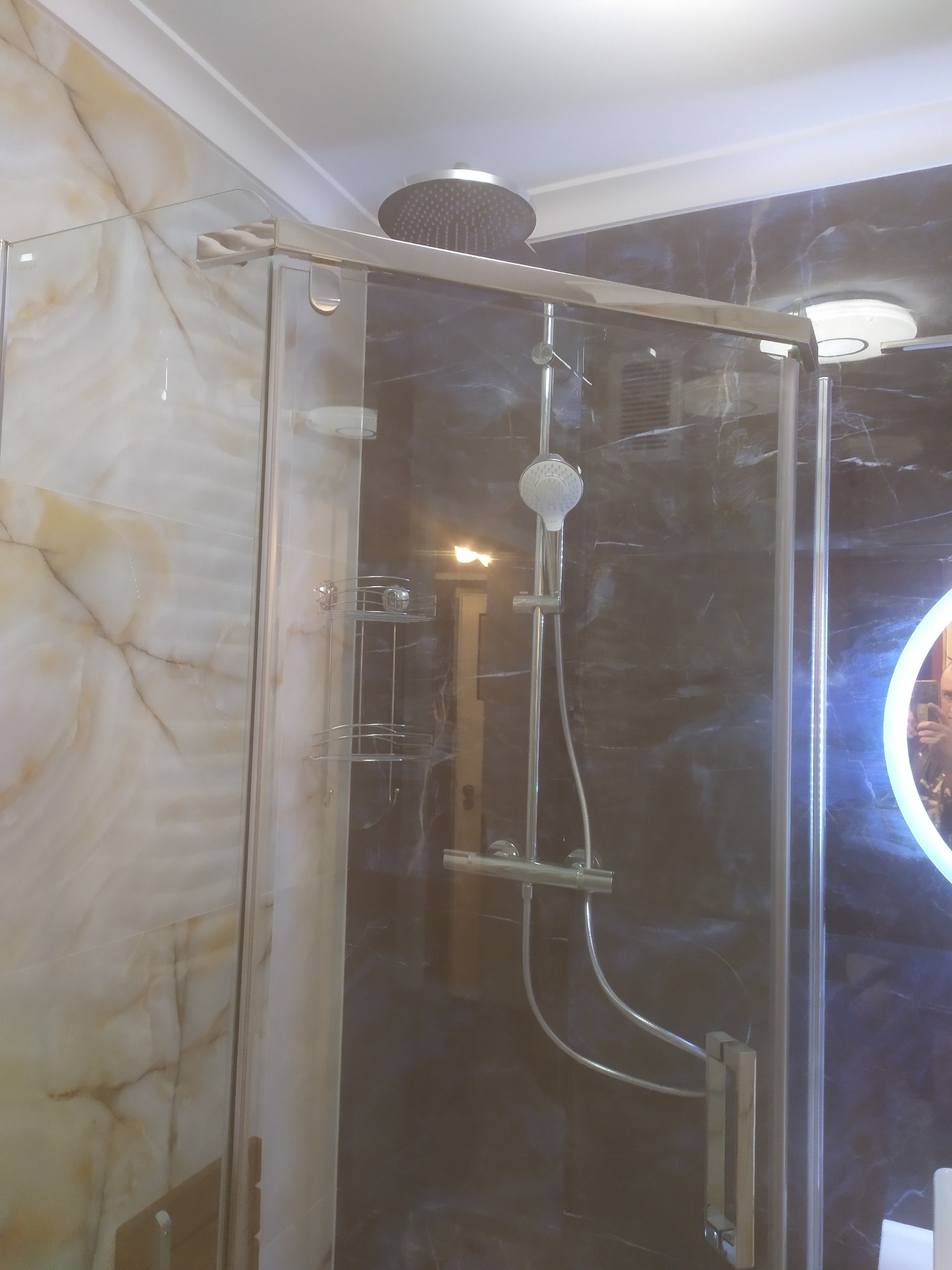 Kabina prysznicowa z deszczownicą i półkami narożnymi, wykończona marmurem w odcieniach beżu i granatu. Realizacja w łazience w Warszawie.