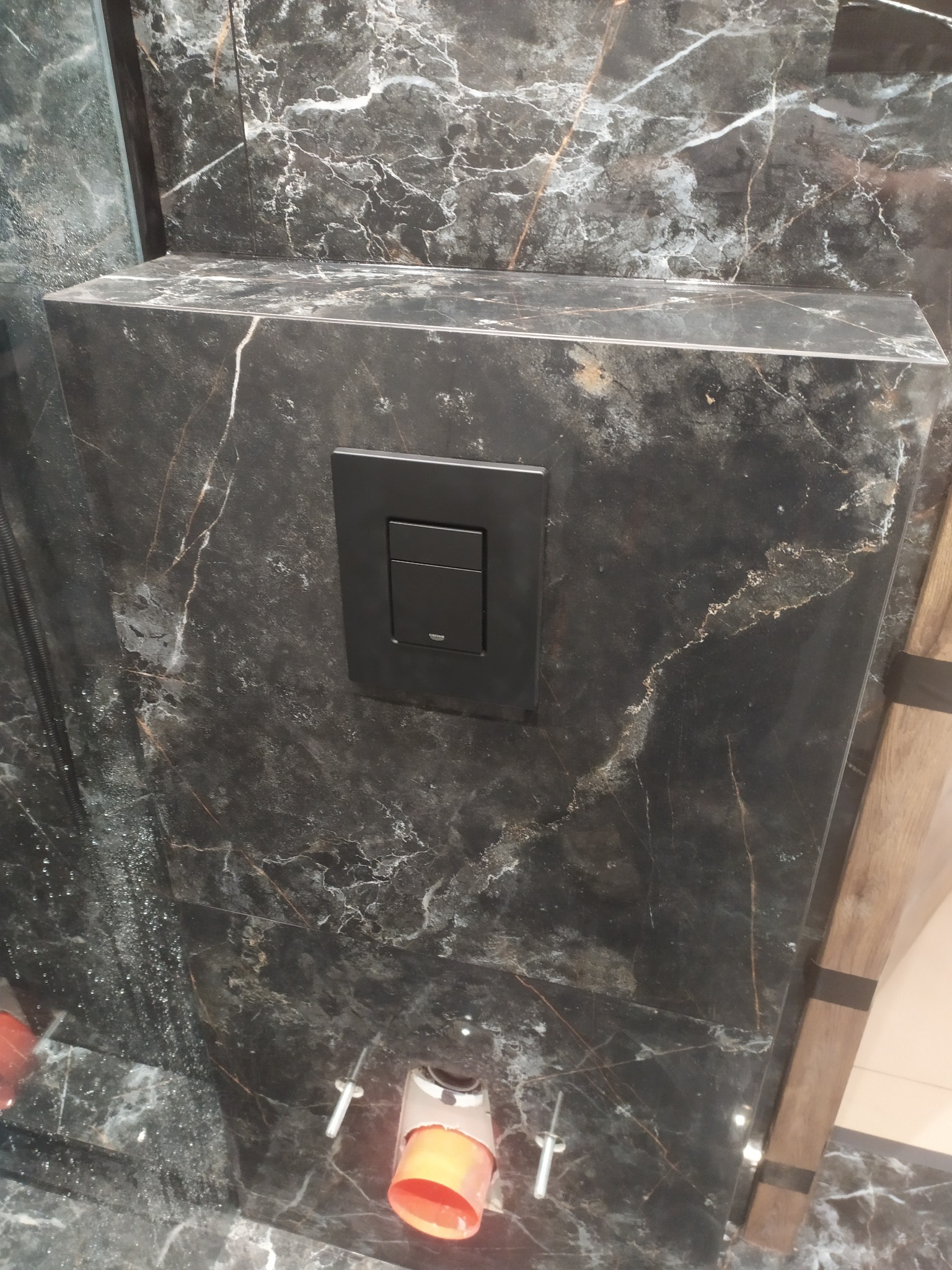 Czarny marmur z czarnym przyciskiem spłuczki w nowoczesnej łazience. Widoczne elementy instalacji podtynkowej.