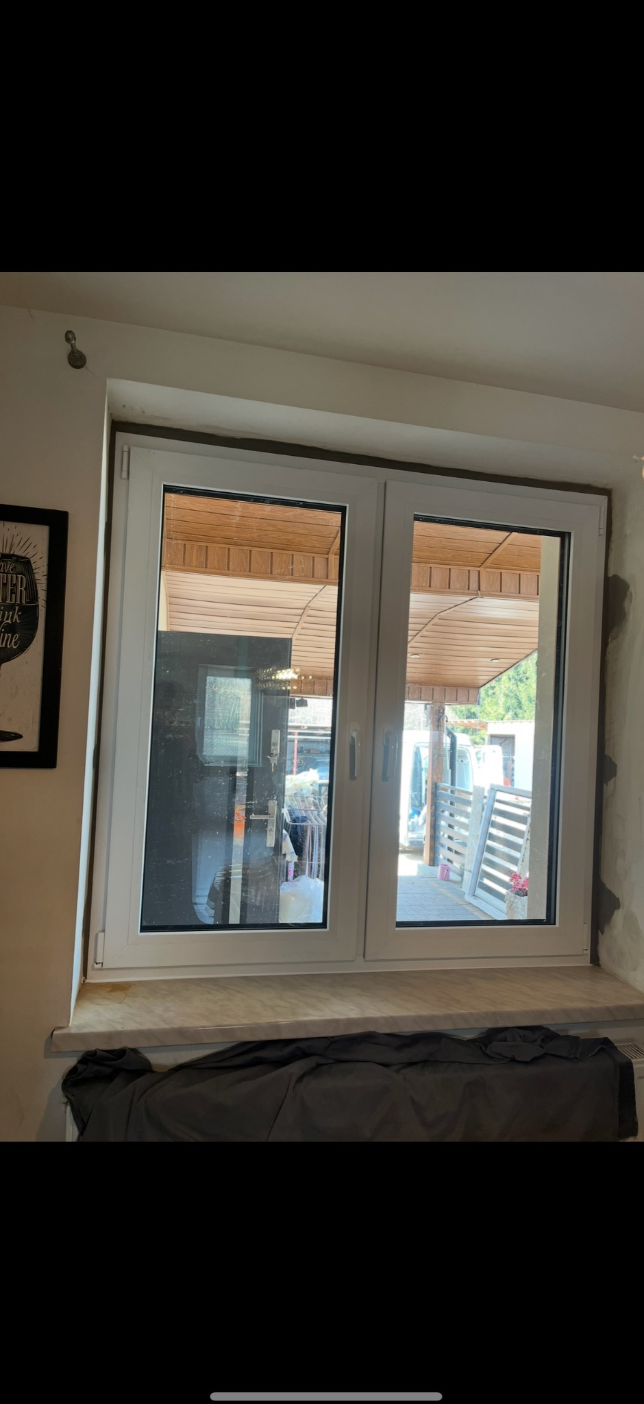 Dwudzielne białe okno PCV z widokiem na podwórze, osłonięte tkaniną na parapecie, z widocznymi śladami prac wykończeniowych na ścianie.