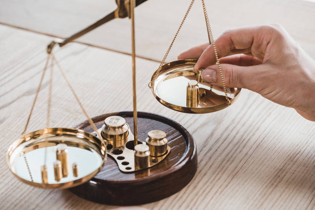Złote wagi szalkowe z odważnikami; dłoń dodaje ciężarek. Symbol sprawiedliwości, równowagi i uczciwości w kontekście finansów i kredytów.