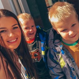 Katarzyna Borkowska - Uśmiechnięta kobieta robi selfie z dwójką roześmianych chłopców w kurtkach na tle jasnego okna. Widoczne detale ubrań i promienny wyraz twarzy.