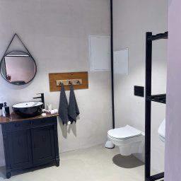 Karpowicz-Korbwaren - Nowoczesna łazienka z szarą posadzką, czarną szafką pod umywalką i minimalistycznym designem. Widoczne elementy: lustro, toaleta podwieszana, ręczniki.