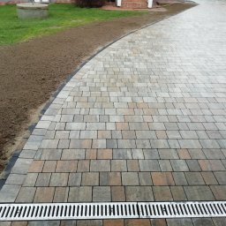 Geo grunt serwis Kraków - Ułożona kostka brukowa w odcieniach szarości i brązu, z widocznym odpływem liniowym i przygotowanym terenem pod trawnik. Nowoczesne i estetyczne wykończenie podjazdu.