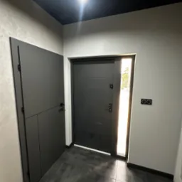 Nowoczesny przedpokój w szarościach: drzwi wejściowe z przeszkleniem, szafa w zabudowie, ciemna podłoga z płytek, kontrastujący czarny sufit i minimalistyczne włączniki.