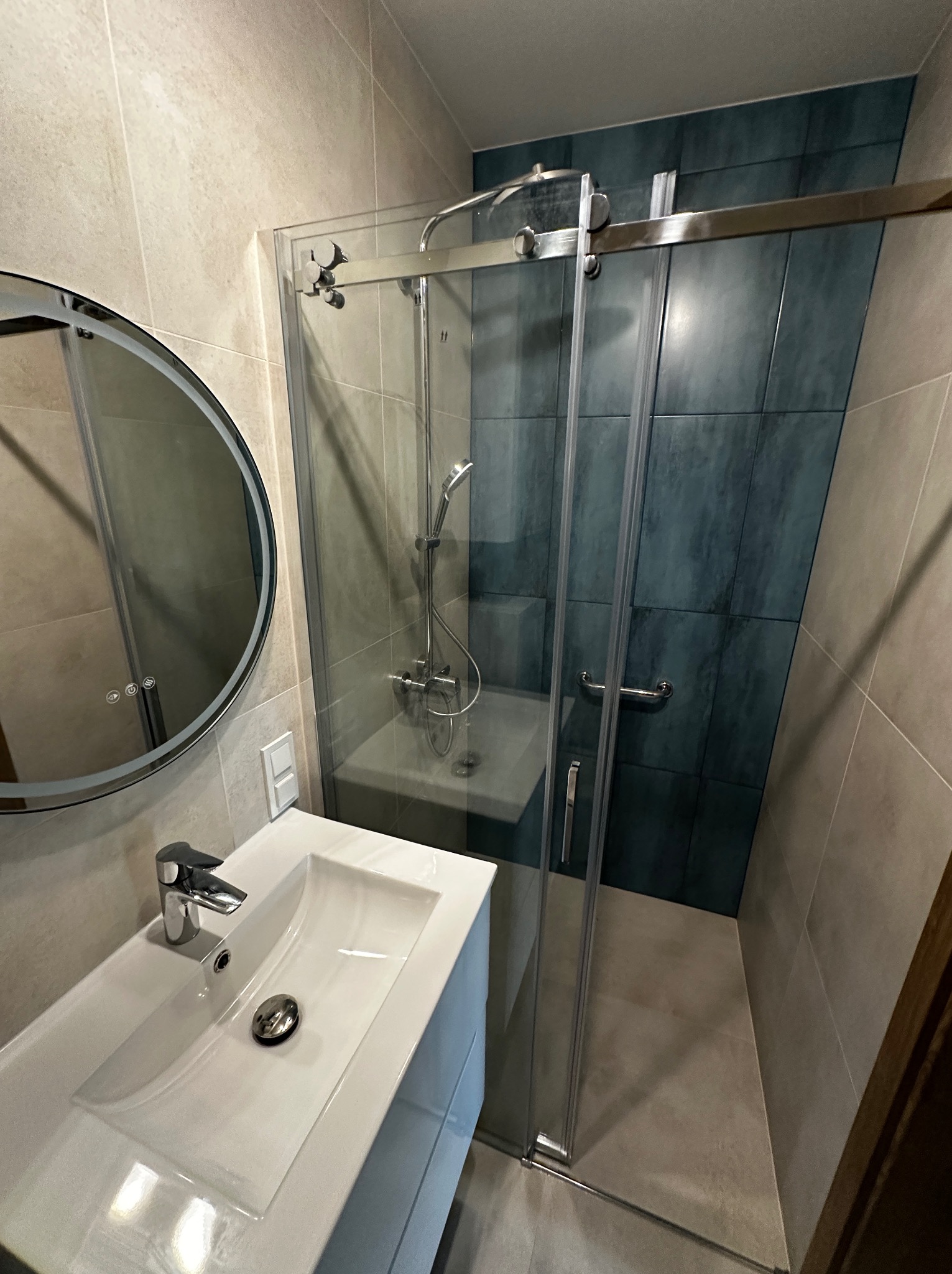 Wykończona łazienka w Zgorzelcu: kabina prysznicowa ze szklanymi drzwiami przesuwnymi, umywalka z szafką i okrągłe lustro z podświetleniem LED.