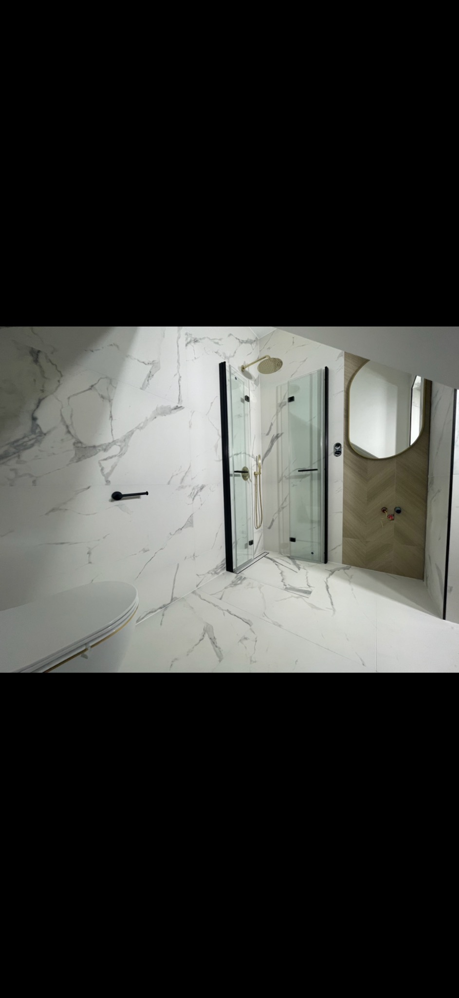 Elegancka łazienka z kabiną prysznicową w czarnej ramie, marmurowymi płytkami i owalnym lustrem z podświetleniem. Nowoczesny wystrój z złotymi akcentami.