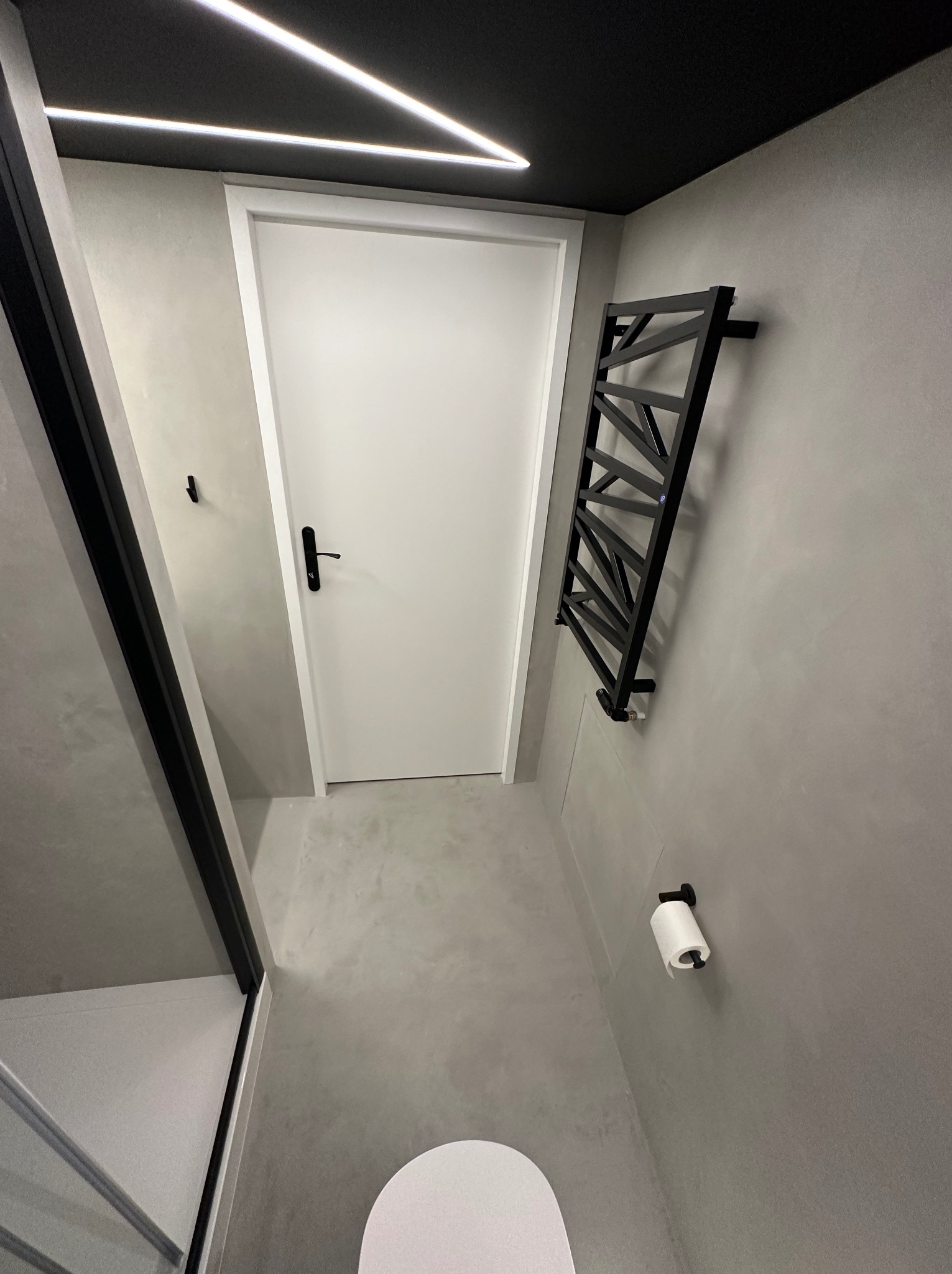 Nowoczesna łazienka z minimalistycznym grzejnikiem drabinkowym w kolorze czarnym, białą armaturą i oświetleniem LED w suficie. Ściany wykończone w szarości.