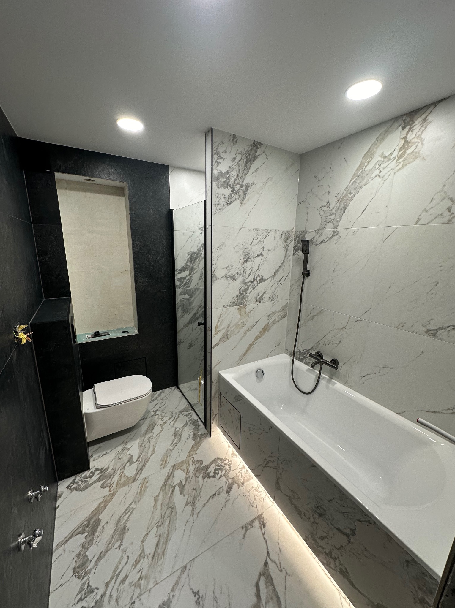 Nowoczesna łazienka z czarno-białymi płytkami imitującymi marmur, białą armaturą i oświetleniem LED pod wanną. Minimalistyczny design z akcentami złota.