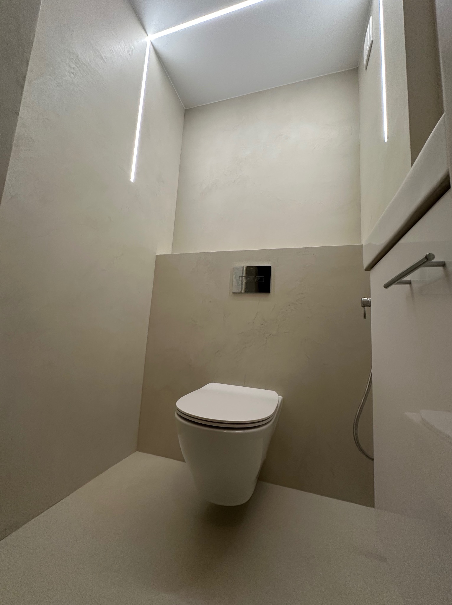 Minimalistyczna toaleta w odcieniach beżu z podtynkową spłuczką i liniowym oświetleniem LED, tworząca nowoczesny i elegancki wystrój wnętrza.