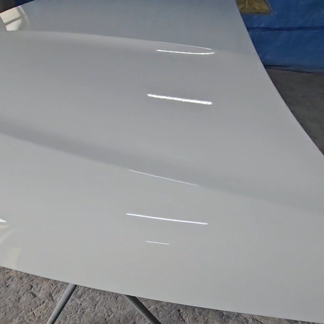 Błyszcząca, biała maska samochodu po lakierowaniu, z widocznymi odbiciami światła. Detal prezentujący gładką powierzchnię i jakość wykonanej usługi.