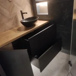 Nowoczesna łazienka z umywalką nablatową i szafką z otwartymi szufladami, drewniany blat, ściana w jodełkę, oświetlona wnęka. Minimalistyczny design.