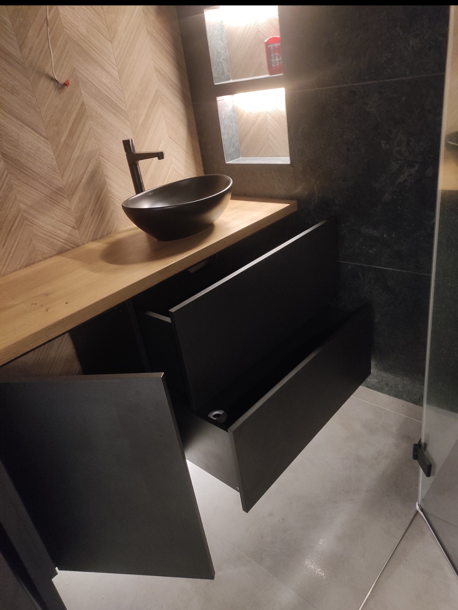 Nowoczesna łazienka z umywalką nablatową i szafką z otwartymi szufladami, drewniany blat, ściana w jodełkę, oświetlona wnęka. Minimalistyczny design.