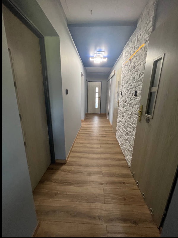 Wykończony korytarz z panelami podłogowymi, szarą ścianą i dekoracyjną ścianą z białej cegły. Sufit pomalowany na niebiesko z nowoczesnym oświetleniem.