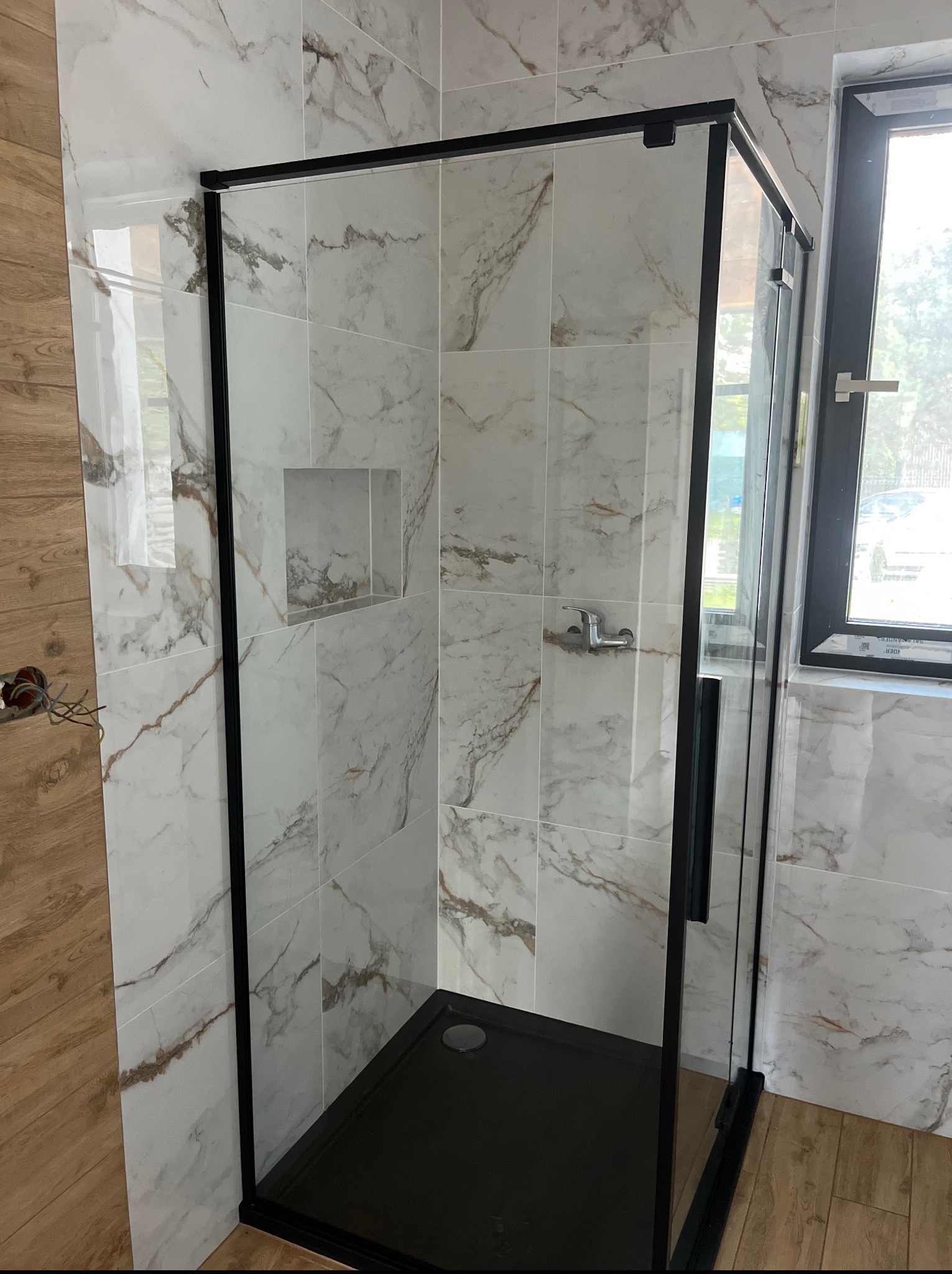 Kabina prysznicowa z czarnymi profilami i marmurowymi płytkami w łazience w Warszawie. Widoczny brodzik i bateria.