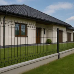 Nowoczesne ogrodzenie panelowe w kolorze grafitowym, z podmurówką, na tle domu z ciemną dachówką i zadbanym trawnikiem. Estetyczne wykończenie posesji.