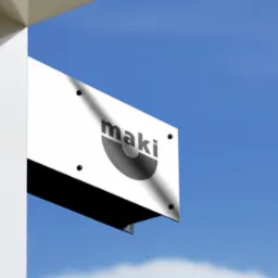Biały szyld reklamowy z czarnym logo 'maki' na tle błękitnego nieba, zamocowany do rogu budynku. Widoczny fragment elewacji i mocowania szyldu.