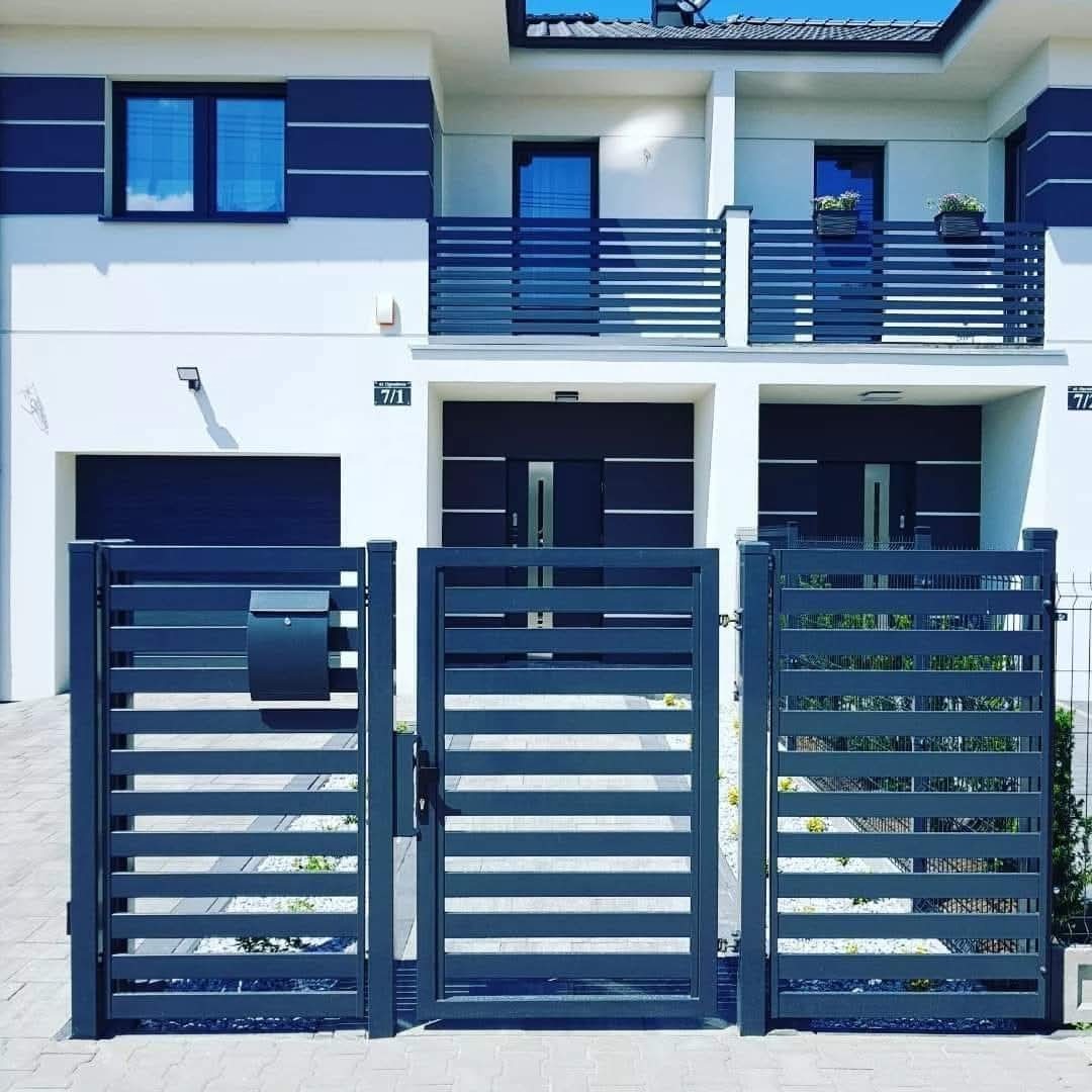 Nowoczesna, pozioma brama metalowa w kolorze grafitowym, z dopasowaną skrzynką na listy, na tle białego domu z balkonami z poziomymi balustradami.