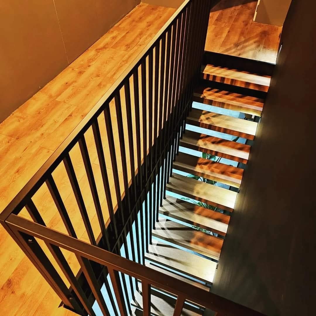 Nowoczesne schody z drewnianymi stopniami i czarną metalową balustradą, widziane z góry. Minimalistyczny design, ciepłe oświetlenie.