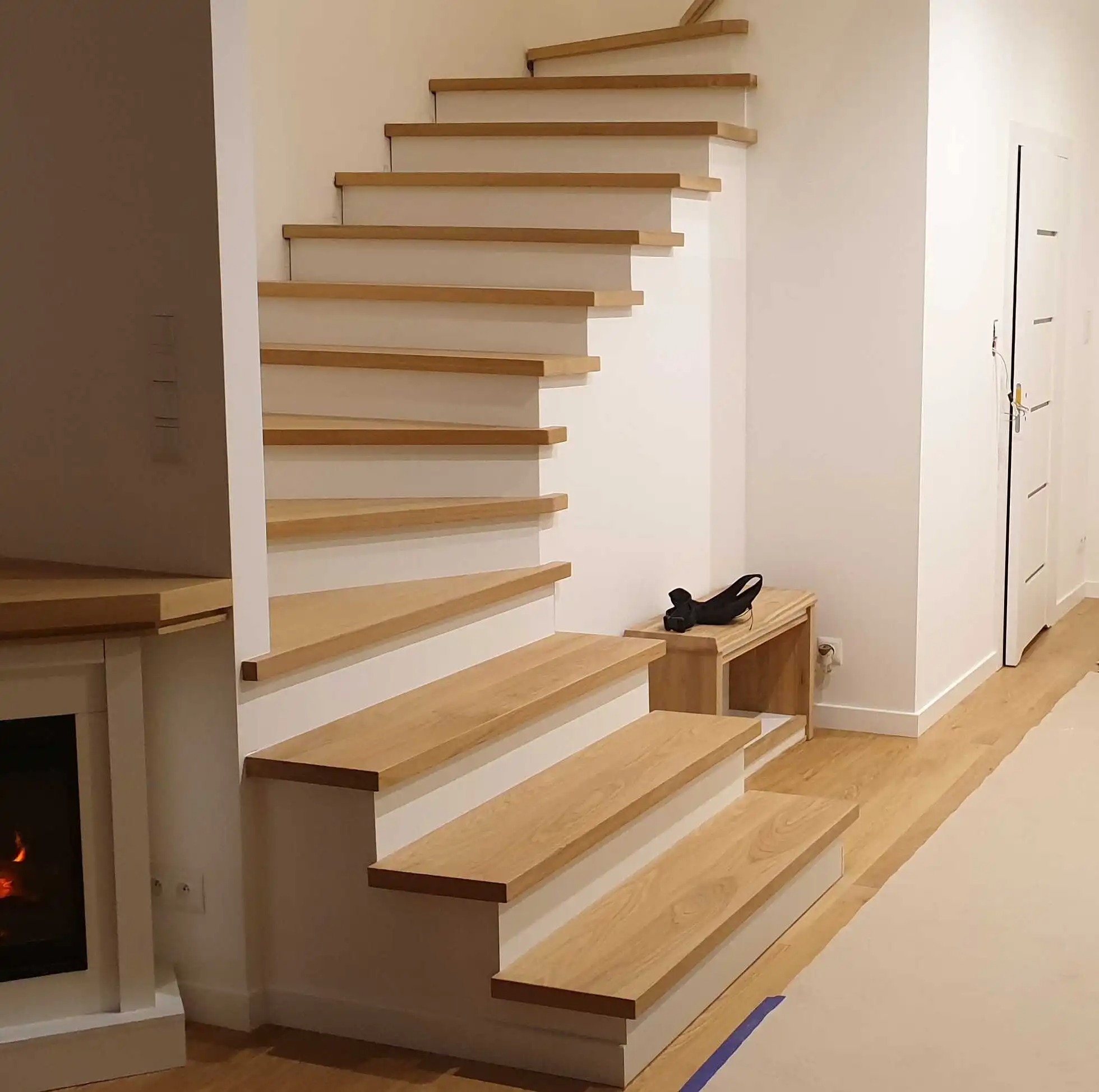 Nowoczesne schody z jasnego drewna i białymi podstopnicami w minimalistycznym wnętrzu. Widoczne detale wykończenia i naturalny odcień drewna.