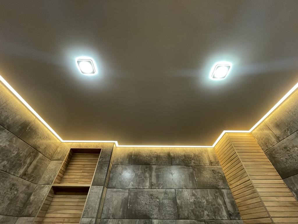 Nowoczesny sufit z oświetleniem LED, podkreślającym geometryczne kształty i fakturę ściany. Dwa kwadratowe punkty świetlne. Wykończenie w odcieniach szarości i beżu.