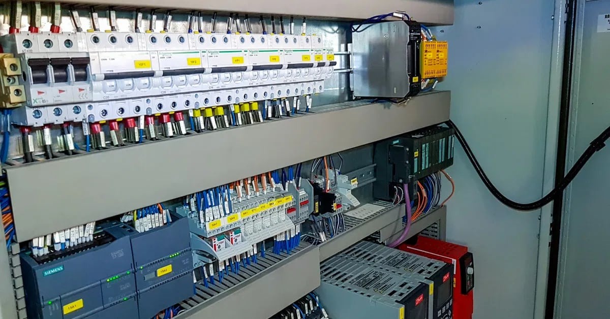 Wnętrze szafy sterowniczej z rozbudowaną instalacją elektryczną, widoczne liczne zabezpieczenia, sterowniki Siemens i okablowanie. Precyzyjny montaż i dbałość o detale.