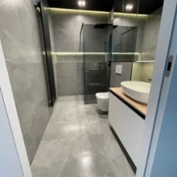 Nowoczesna łazienka w odcieniach szarości z czarnymi akcentami, podświetleniem LED i kabiną prysznicową typu walk-in. Minimalistyczny design z umywalką nablatową.