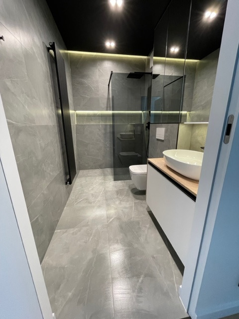 Nowoczesna łazienka w odcieniach szarości z czarnymi akcentami, podświetleniem LED i kabiną prysznicową typu walk-in. Minimalistyczny design z umywalką nablatową.